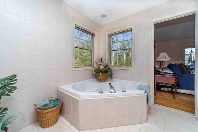 bathroom with tiled tub, tile patterned flooring, and tile walls