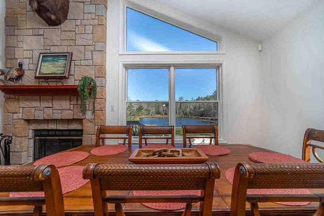 dining space with a stone fireplace, a water view, and vaulted ceiling