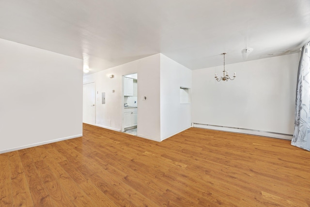 spare room featuring a baseboard heating unit, light hardwood / wood-style floors, and a notable chandelier