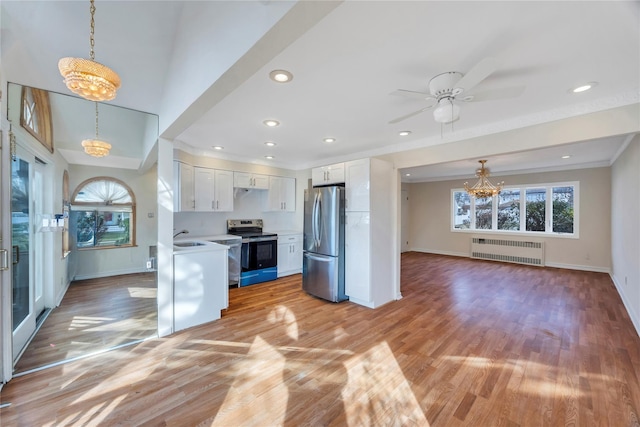 kitchen with appliances with stainless steel finishes, light wood-type flooring, pendant lighting, radiator heating unit, and white cabinetry