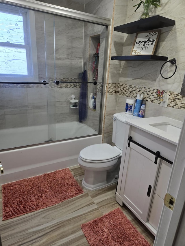 full bathroom with tasteful backsplash, bath / shower combo with glass door, toilet, vanity, and tile walls