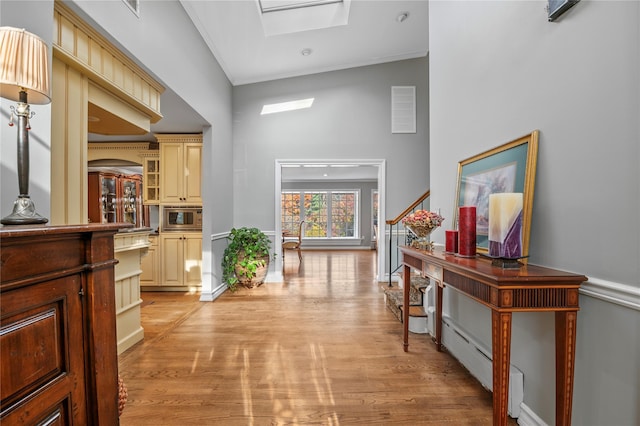 corridor featuring a high ceiling, ornamental molding, light hardwood / wood-style floors, and a skylight