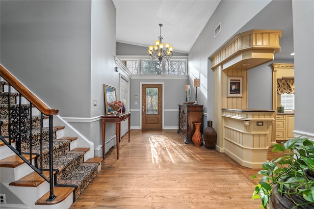 foyer with baseboard heating, high vaulted ceiling, crown molding, a chandelier, and light hardwood / wood-style floors