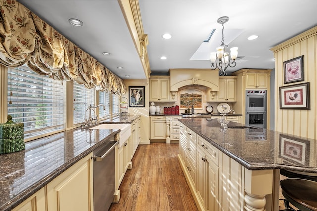 kitchen featuring appliances with stainless steel finishes, dark stone counters, sink, hanging light fixtures, and a breakfast bar area