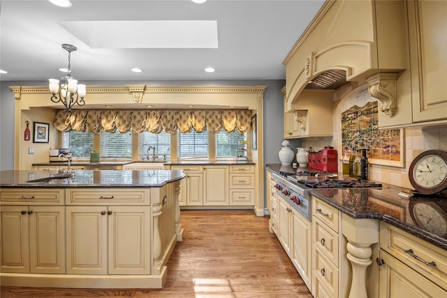 kitchen featuring cream cabinets, a skylight, hanging light fixtures, and dark stone countertops