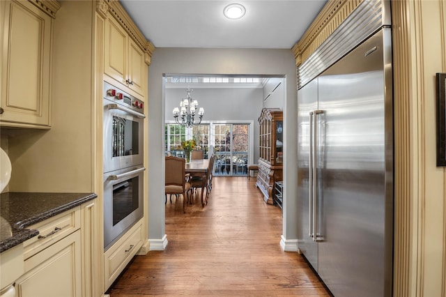 kitchen featuring pendant lighting, dark stone counters, an inviting chandelier, light wood-type flooring, and stainless steel appliances