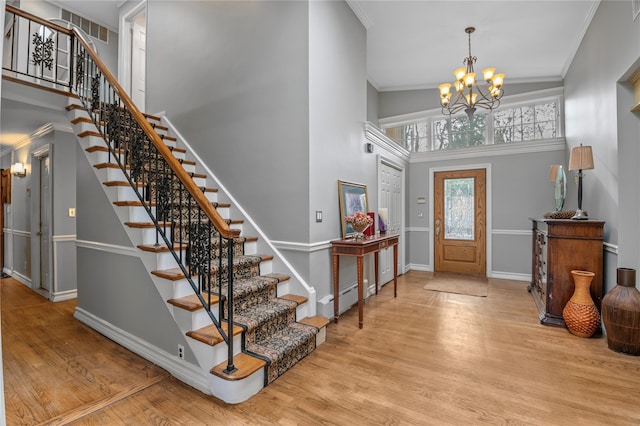 foyer with a notable chandelier, a towering ceiling, crown molding, and light hardwood / wood-style flooring