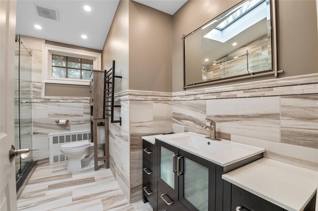 bathroom featuring a skylight, vanity, tile walls, radiator heating unit, and toilet