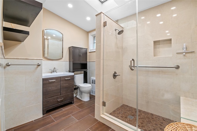 bathroom with vanity, a shower with door, toilet, and tile walls