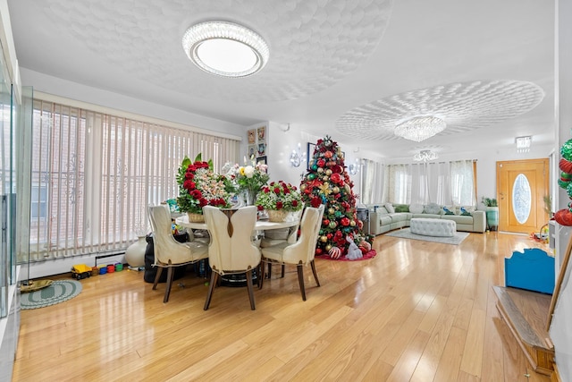 dining space featuring a textured ceiling, light hardwood / wood-style flooring, baseboard heating, and a notable chandelier