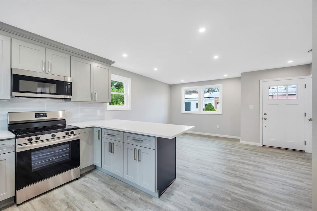 kitchen with kitchen peninsula, stainless steel appliances, a wealth of natural light, and gray cabinetry