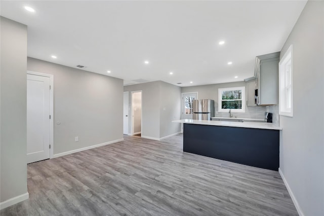 kitchen with gray cabinets, stainless steel fridge, kitchen peninsula, and light hardwood / wood-style floors