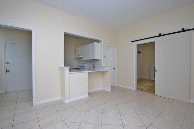 kitchen with white cabinets, decorative backsplash, a barn door, and light tile patterned floors