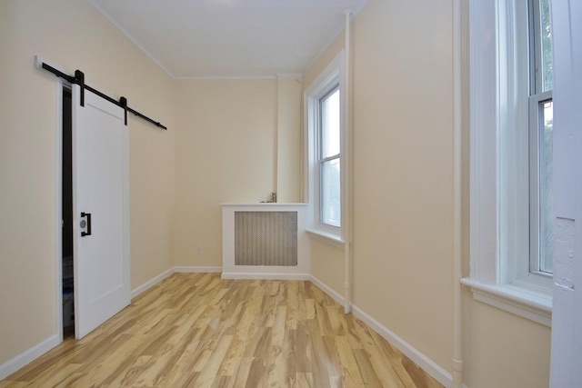 spare room with a barn door, light hardwood / wood-style flooring, and ornamental molding