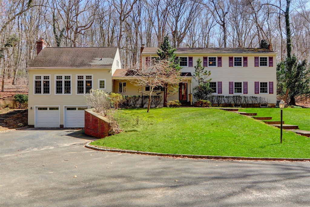 colonial inspired home with a front yard, aphalt driveway, a garage, and a chimney