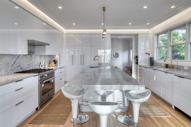 kitchen featuring stainless steel range, a center island with sink, white cabinets, and sink