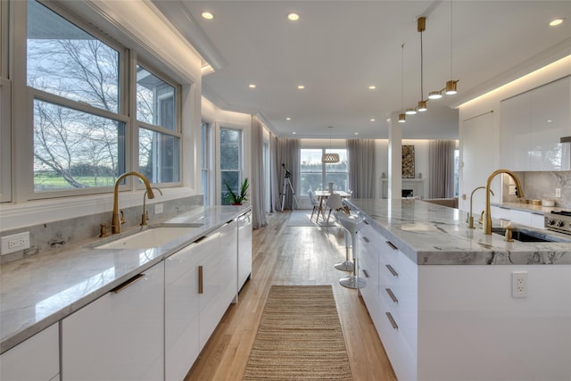 kitchen featuring light stone countertops, white cabinetry, sink, and a large island with sink