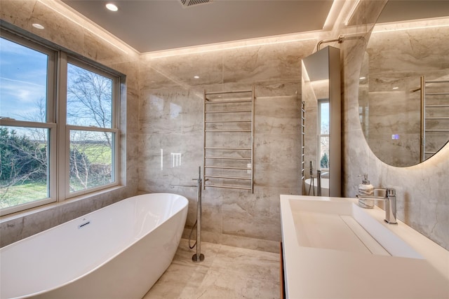 bathroom featuring vanity, a bath, and tile walls