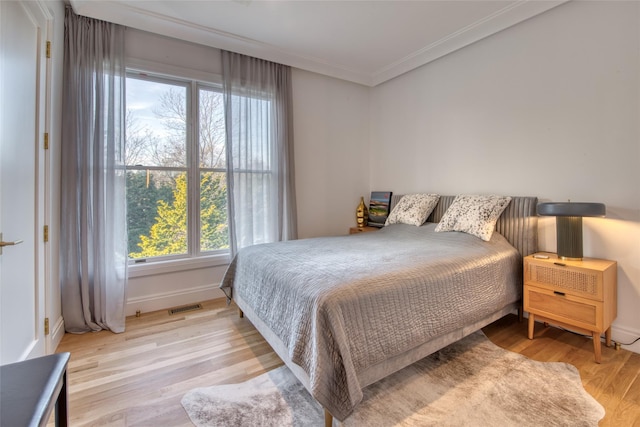 bedroom with ornamental molding and light hardwood / wood-style floors