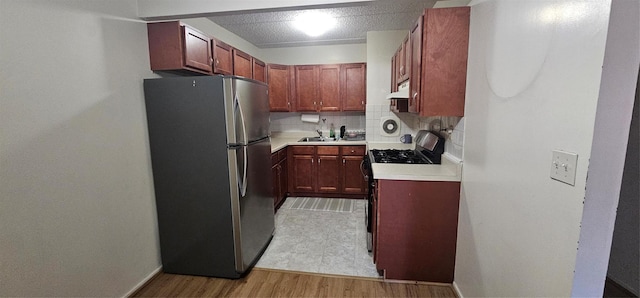 kitchen featuring stainless steel fridge, light wood-type flooring, backsplash, ventilation hood, and range with gas stovetop