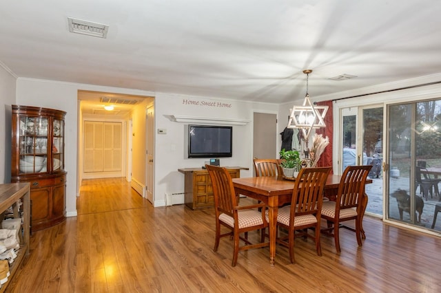 dining area featuring hardwood / wood-style floors, a baseboard heating unit, ornamental molding, and a notable chandelier