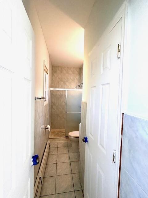 bathroom featuring tile patterned flooring, toilet, baseboard heating, tile walls, and a shower with shower door