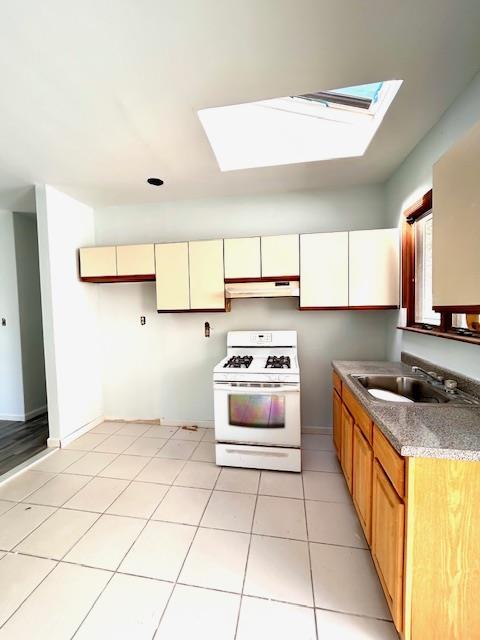 kitchen featuring a skylight, gas range gas stove, sink, and light tile patterned floors