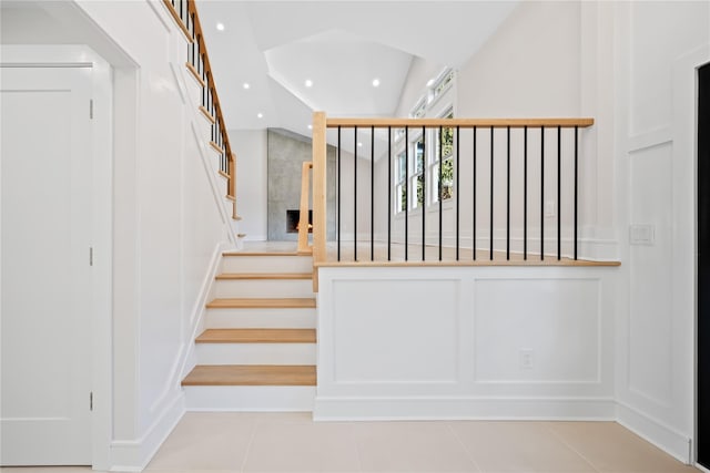 stairs featuring a tile fireplace, tile patterned flooring, and lofted ceiling