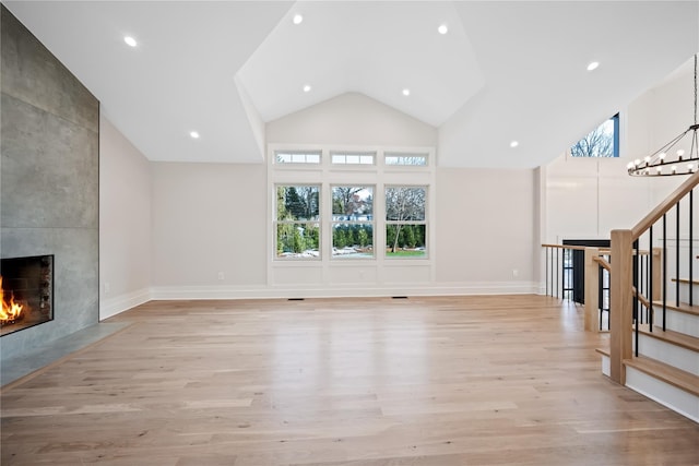 unfurnished living room with a tile fireplace, high vaulted ceiling, light hardwood / wood-style floors, and a notable chandelier