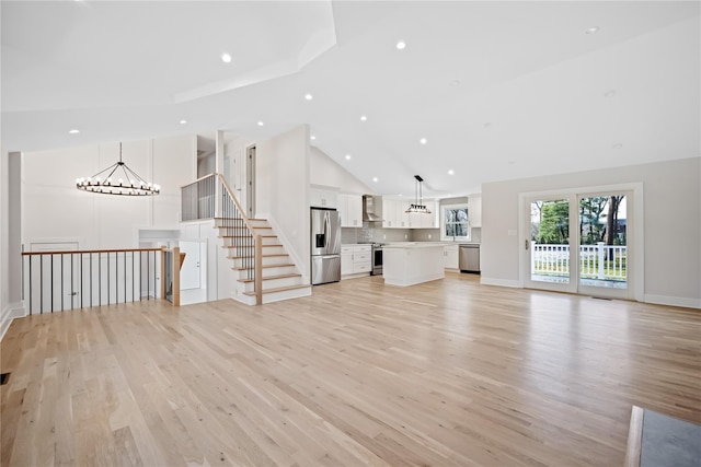 unfurnished living room featuring high vaulted ceiling, light hardwood / wood-style flooring, and a notable chandelier