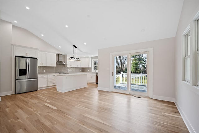 kitchen with wall chimney exhaust hood, hanging light fixtures, stainless steel appliances, a kitchen island, and white cabinets