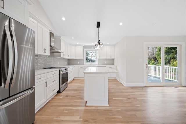 kitchen featuring wall chimney exhaust hood, decorative light fixtures, light hardwood / wood-style floors, white cabinetry, and stainless steel appliances