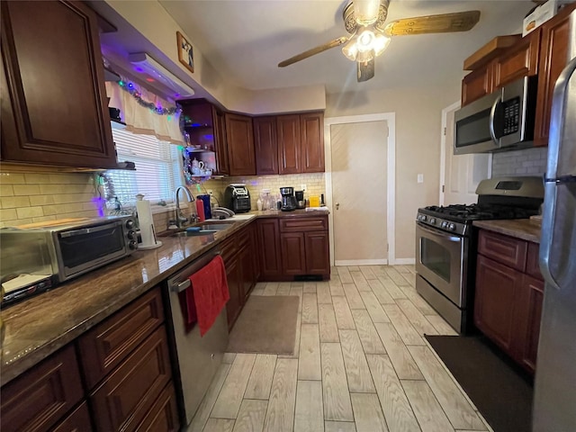 kitchen featuring sink, stainless steel appliances, tasteful backsplash, dark stone counters, and light wood-type flooring