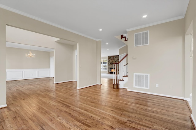 unfurnished living room featuring a notable chandelier, light wood-type flooring, and ornamental molding