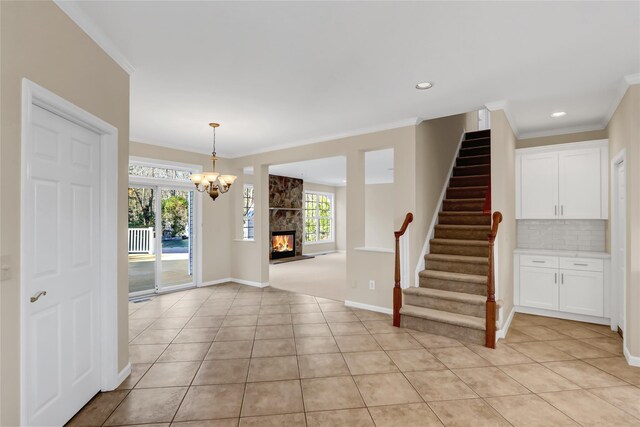 entryway featuring a stone fireplace, a notable chandelier, crown molding, and light tile patterned flooring