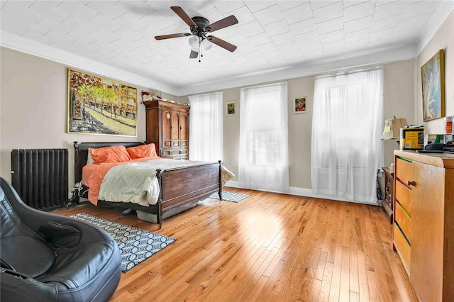 bedroom featuring ceiling fan, radiator heating unit, crown molding, and light wood-type flooring