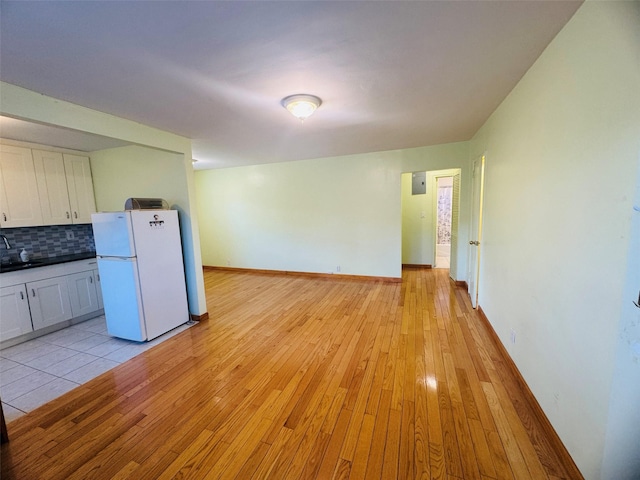 kitchen with white cabinets, light wood-type flooring, white refrigerator, and backsplash