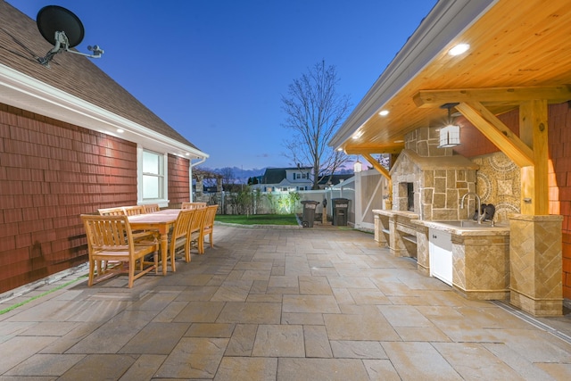 patio terrace at dusk featuring an outdoor stone fireplace and area for grilling