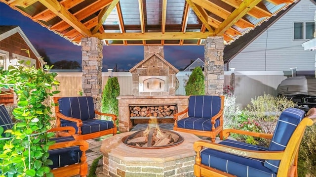 patio terrace at dusk with an outdoor stone fireplace, a fire pit, and a gazebo