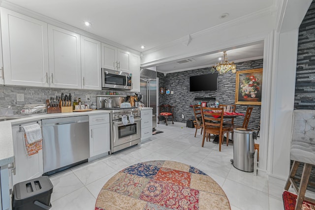 kitchen featuring white cabinets, decorative backsplash, ornamental molding, appliances with stainless steel finishes, and a chandelier