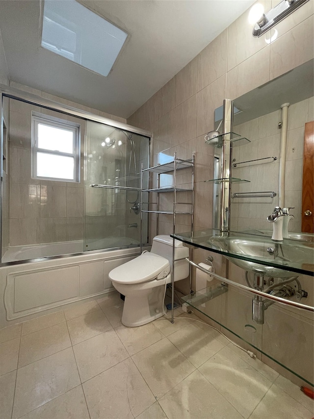 full bathroom featuring tile patterned floors, bath / shower combo with glass door, sink, tile walls, and toilet