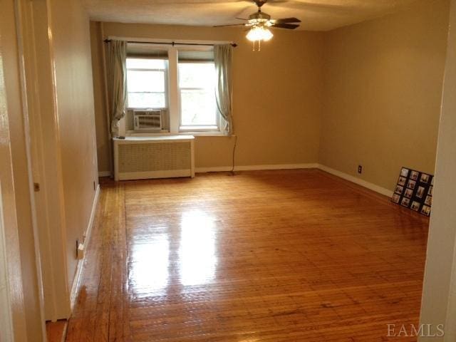 spare room featuring ceiling fan, radiator heating unit, cooling unit, and light hardwood / wood-style flooring