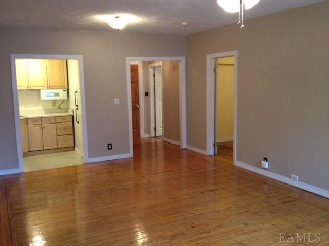 unfurnished bedroom with ensuite bath, a spacious closet, light hardwood / wood-style floors, a textured ceiling, and a closet