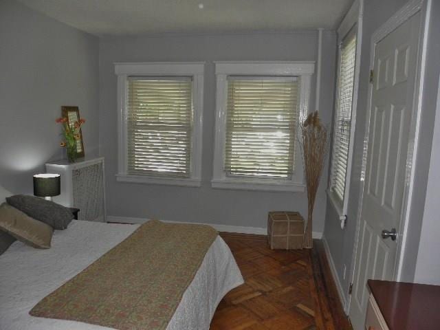 bedroom with dark parquet floors and multiple windows