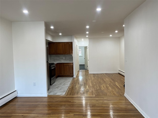 kitchen featuring decorative backsplash, light wood-type flooring, appliances with stainless steel finishes, and a baseboard radiator