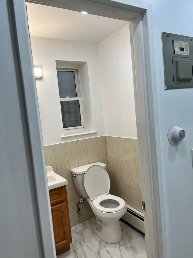 bathroom featuring vanity, baseboard heating, tile walls, electric panel, and toilet