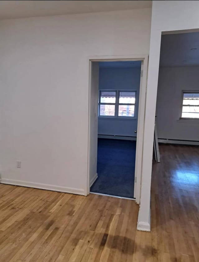 empty room featuring hardwood / wood-style floors, baseboard heating, and plenty of natural light