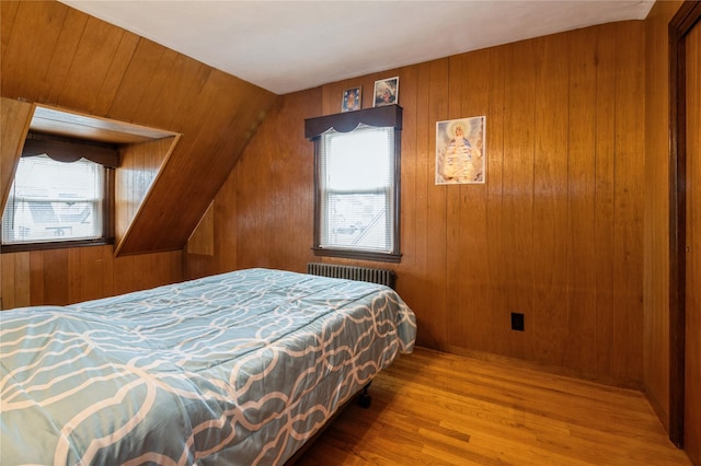 bedroom with radiator heating unit, hardwood / wood-style flooring, vaulted ceiling, and wood walls