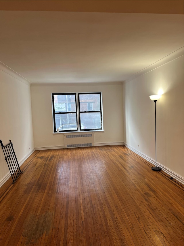 empty room featuring radiator heating unit, ornamental molding, and hardwood / wood-style flooring