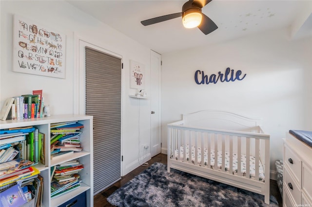 bedroom featuring ceiling fan, dark wood-type flooring, and a crib